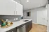 Modern kitchen with sleek white cabinetry, elegant backsplash, and light wood flooring, featuring a stainless steel dishwasher and stylish accessories.