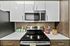 Modern kitchen with sleek white cabinets, stainless steel microwave, and oven, accented by decorative jars and a vase of fresh flowers on a pristine countertop.
