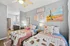 Charming bedroom with twin beds adorned with colorful quilts and whimsical pillows, featuring vibrant wall art and a cozy desk area with warm lighting.