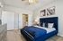 Modern bedroom featuring a luxurious blue velvet bed, elegant artwork, and natural light highlighting a sophisticated design. | Legacy at Crowley | Atlanta Apartments
