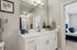 Modern bathroom with elegant white vanity, large mirror, and sleek fixtures, opening into a cozy bedroom with plush blue accents.