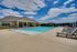 Inviting outdoor pool area with comfortable lounge chairs and a modern clubhouse under a bright blue sky.