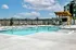Luxurious apartment complex pool area with crystal-clear water, inviting lounge chairs, and a stylish pergola under a bright, sunny sky.