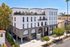 Elegant modern apartment building with striking arched windows, rooftop terrace, and lush landscaping in a vibrant urban setting.
