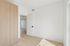 Bright and airy bedroom with natural wood flooring, built-in light wood wardrobe, and modern white door opening to a spacious area.