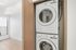 Bright and modern apartment with a convenient in-unit laundry area featuring a stacked washer and dryer, adjacent to a sunlit room with sleek wooden floors.