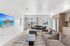 Modern living room with sleek design, featuring a comfortable sofa, wall-mounted TV, and views of palm trees through large windows.