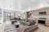 Bright open-concept living space with a stylish modern kitchen, luxurious seating area, and elegant dining set near large windows.