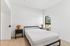 Bright and airy bedroom with minimalist decor, featuring a large window, sleek bed frame, and stylish rattan lamps.