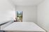 Bright, minimalist bedroom featuring a large window with scenic views, complemented by a cozy, modern bed setup for ultimate relaxation.
