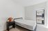 Bright and modern bedroom with a minimalist design, featuring a sleek black bed frame, cozy side table with a woven lamp, and ample natural light through a large window.