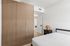 Modern apartment bedroom with sleek wooden closet, stylish lamp, and minimalist decor.