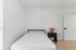 Bright and minimalist bedroom featuring a cozy bed, sleek wooden flooring, and a stylish nightstand with a decorative lamp.