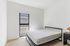 Bright, minimalist bedroom with large window and modern furnishings, offering a serene living space.