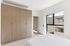 Bright bedroom featuring a large built-in wooden wardrobe and a window offering a pleasant view of neighboring apartments.