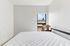 Bright bedroom with minimalist decor, featuring a cozy bed, a sleek wooden nightstand, and a large window offering a stunning view.
