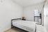 Bright and modern bedroom featuring a sleek bed frame, stylish side table with a unique lamp, large wardrobe, and natural light streaming through the large window.