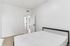 Bright and airy bedroom featuring a modern minimalistic design with light wood flooring and a chic bed frame, leading to an inviting hallway.