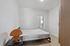 Bright and minimalist bedroom with a cozy bed, wooden flooring, and a unique wicker lamp on a bedside table.