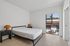 Elegant bedroom with minimalist decor, featuring a cozy bed, two stylish nightstands, and a large window offering scenic views of palm trees and rooftops.