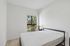 Cozy bedroom with a large window and serene outdoor view, featuring minimalistic decor and a warm, inviting ambiance.