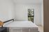 Bright, minimalist bedroom with large window and leafy view, featuring a cozy bed and sleek modern design.