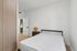 Bright and modern bedroom with minimalist design, featuring a comfortable bed, elegant wooden wardrobe, and stylish bedside table with a unique lamp.