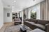 Bright and inviting living room with modern furniture, large arched windows, and an open-concept kitchen in the background, offering a seamless blend of comfort and style.