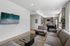 Modern living room with elegant decor, featuring a mounted flat-screen TV, cozy gray sofa set, and a sleek kitchen with stainless steel appliances in the background.