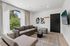 Bright living room with modern gray couches, large windows offering garden views, and stylish wall art for a cozy ambiance.