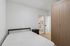 Bright, modern bedroom with minimalist design and ensuite bathroom, featuring sleek wooden wardrobe and light wooden flooring.