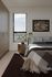 Cozy bedroom with large window view, elegant bedding, wooden nightstand, and modern abstract art.