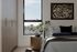 Inviting bedroom with modern decor, featuring a large window with skyline views, elegant wooden wardrobe, and stylish bedside table.