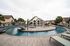Luxurious apartment complex with a resort-style swimming pool, beautiful bridge, and inviting lounge chairs amidst lush palm trees.