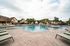 Luxurious swimming pool area with stylish lounge chairs and scenic view of beautifully designed homes and lush greenery.