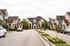 Charming residential street lined with elegant stone houses, manicured gardens, and lush greenery, creating a welcoming and serene neighborhood ambiance.