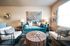 Cozy living room with a stylish teal sofa, modern chairs, and a rustic wooden coffee table, accented by large artwork and warm lighting.