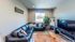 Inviting living room with stylish L-shaped leather sofa, large TV, and cozy decor, enhanced by a potted plant and natural light from the window.