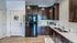 Charming modern kitchen with dark wooden cabinets, sleek black fridge, and elegant countertops, featuring a welcoming wreath on the door.