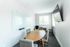 Modern meeting room with a sleek wooden table, stylish chairs, large whiteboard, and a wall-mounted flat-screen TV.