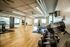 Modern fitness studio with wooden floors featuring an array of dumbbells, exercise bikes, and large windows for natural light.