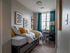 Inviting bedroom with a cozy single bed, vibrant pillows, modern art, and a window view, creating a peaceful retreat.