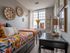 Charming bedroom with vibrant floral bedding, stylish decor, and natural light pouring through a large window, creating a cozy and inviting study nook.