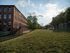 Charming brick building beside a lush green space under a bright blue sky with scattered clouds.