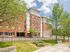 Charming university housing building with red brick facade, lush green trees, and clear blue skies. Perfect blend of modern living and academic ambiance.