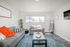 Bright and inviting living room featuring stylish gray sofas, a vibrant orange throw, and a modern blue rug accenting a cozy, contemporary atmosphere.