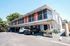 Modern two-story apartment building with vibrant orange doors, ample parking, and lush greenery.