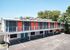 Modern apartment building with vibrant orange doors, surrounded by lush greenery and ample parking. Ideal urban living with stylish exterior design.