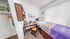 Cozy bedroom with a single bed, a tidy study desk, and ample natural light from large window blinds.