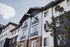 Modern apartment exterior with elegant balconies, lush greenery, and stylish architecture against a clear sky backdrop.